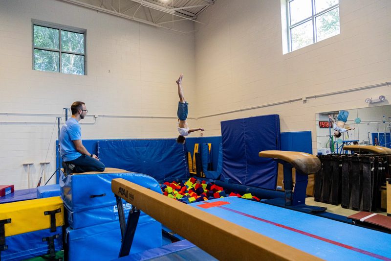 Young Arlington Tigers gymnast vaulting into foam pit with coach watching at Barcroft